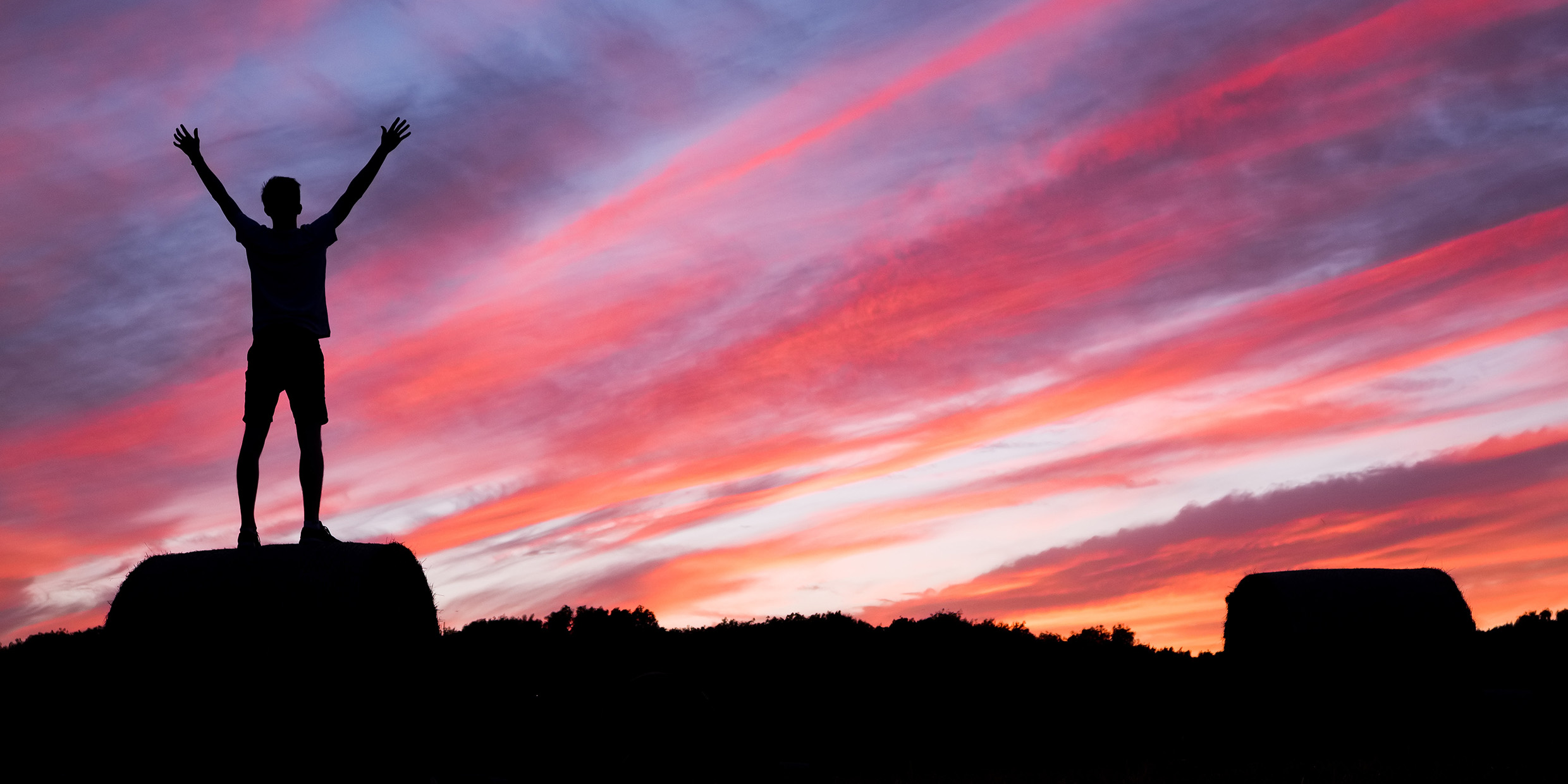 Image of man with arms raised at sunset