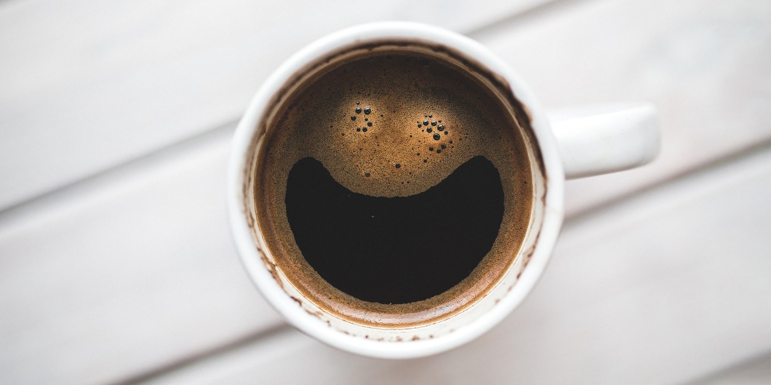 Image of coffee mug with what looks like a smiling face in the froth