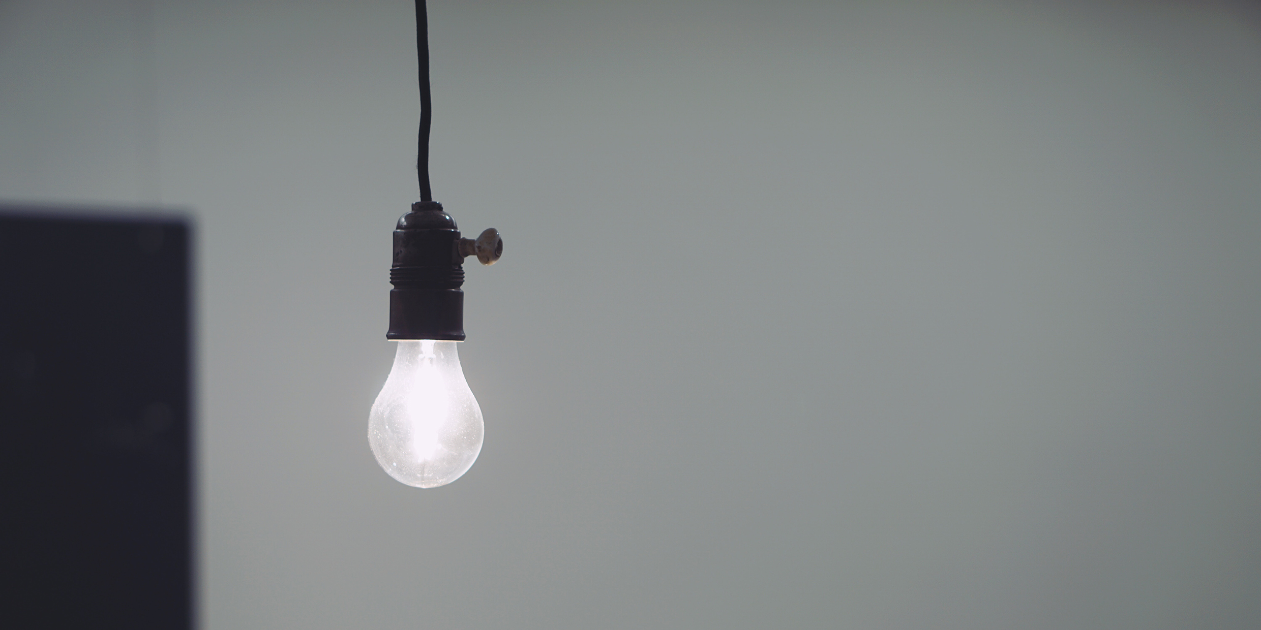 Image of single lit lightbulb hanging in front of white background