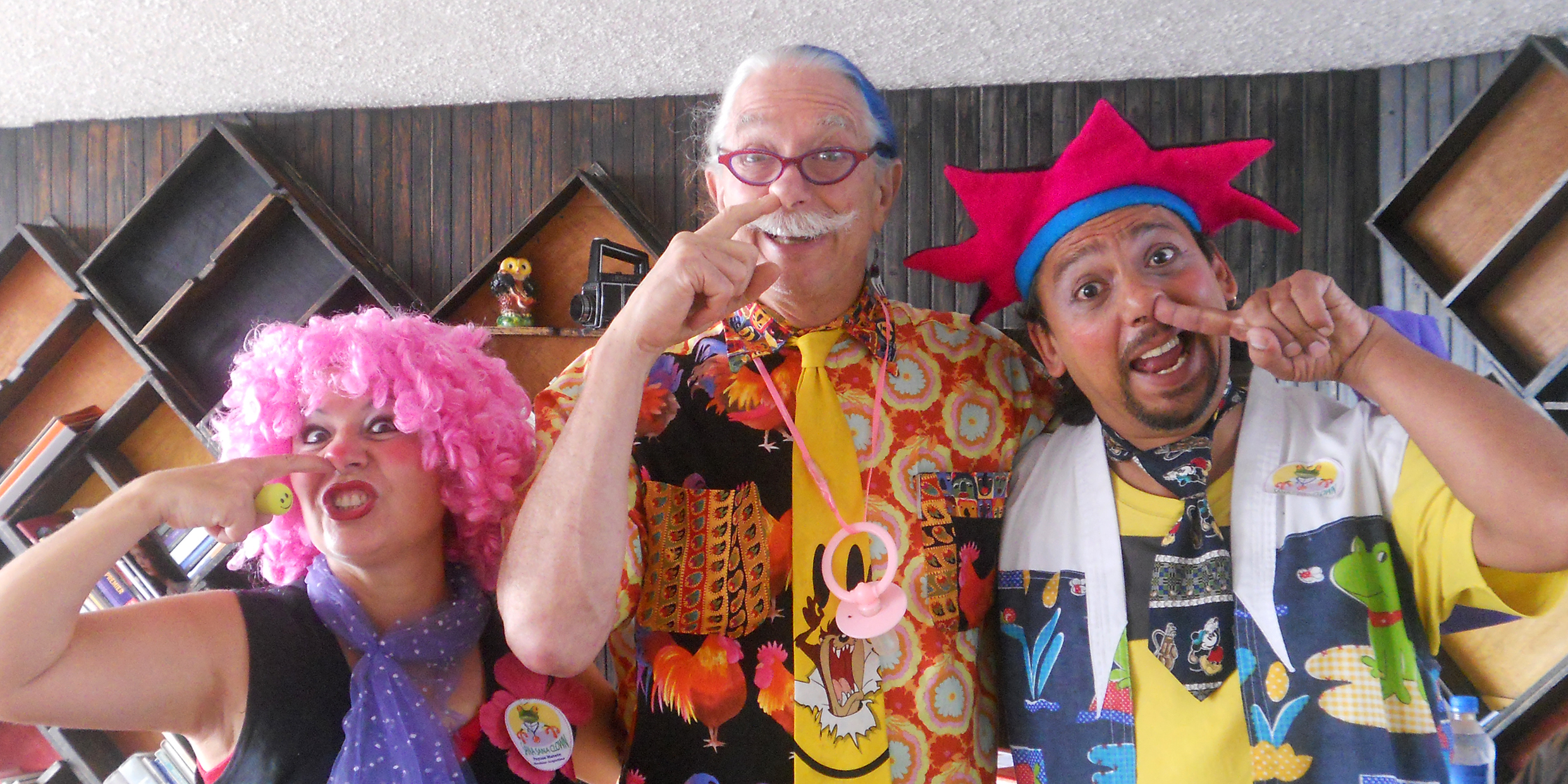 Image of three people in eccentric clothes with their fingers in their noses