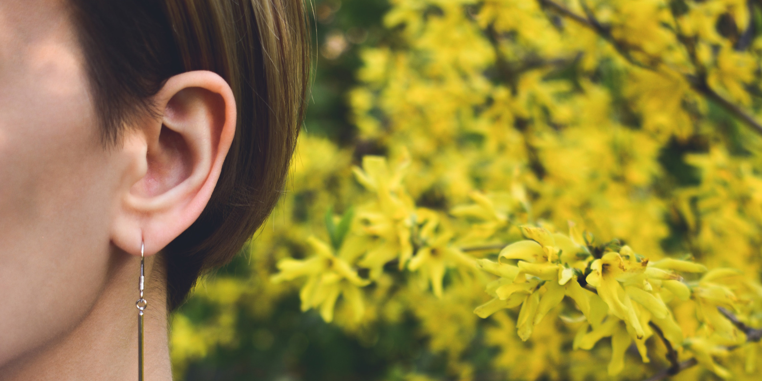 Close-up image of woman's ear with flowers in the background
