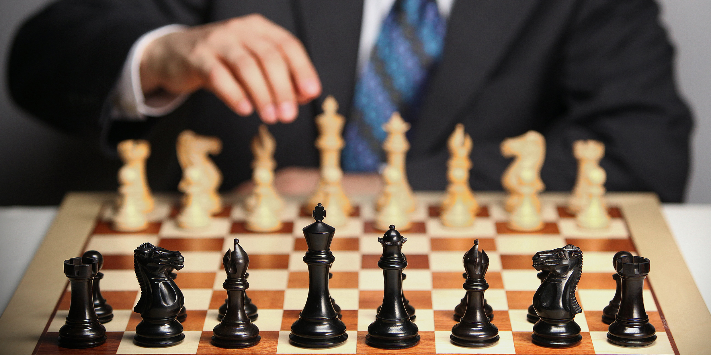 Image of man in suit making opening move at a chess board