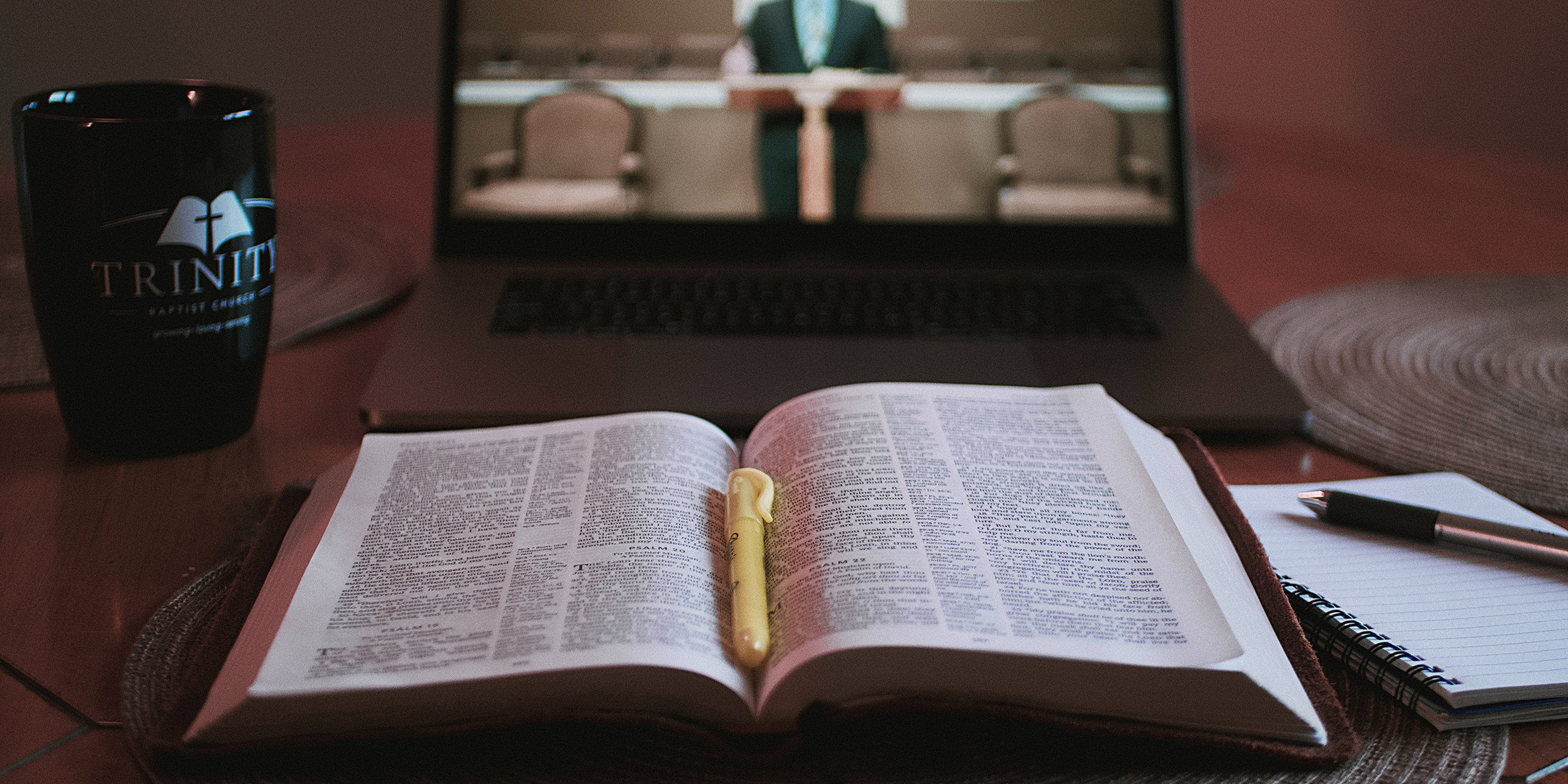 Image of an opened bible in front of a computer laptop livestreaming a church sermon