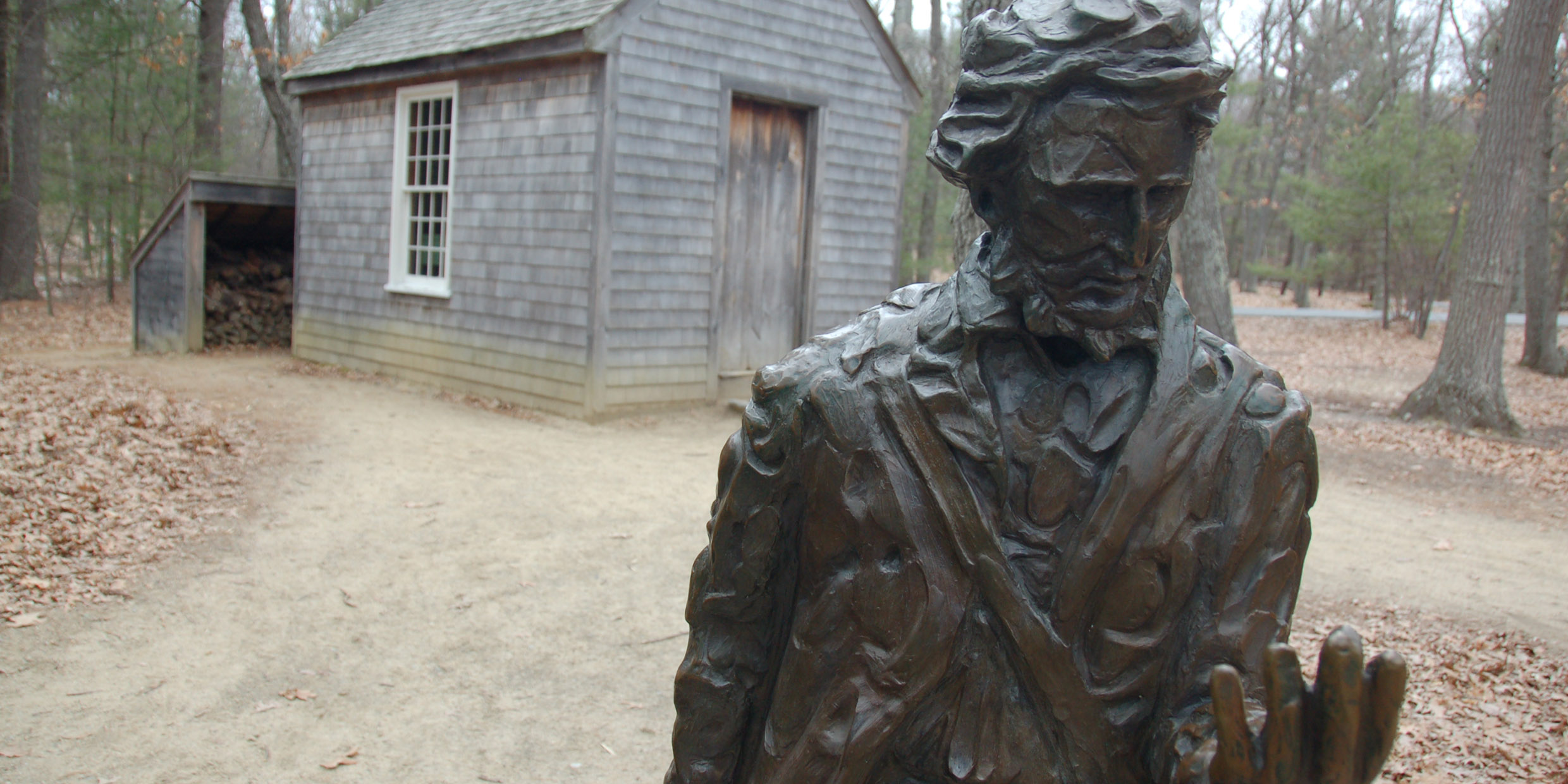 Image of a statue of Throeau in front a replica of his Walden cabin