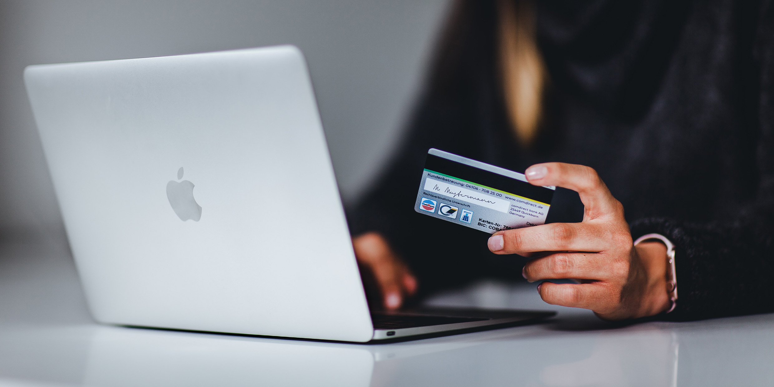 Image of a person holding a credit card seated in front of a computer