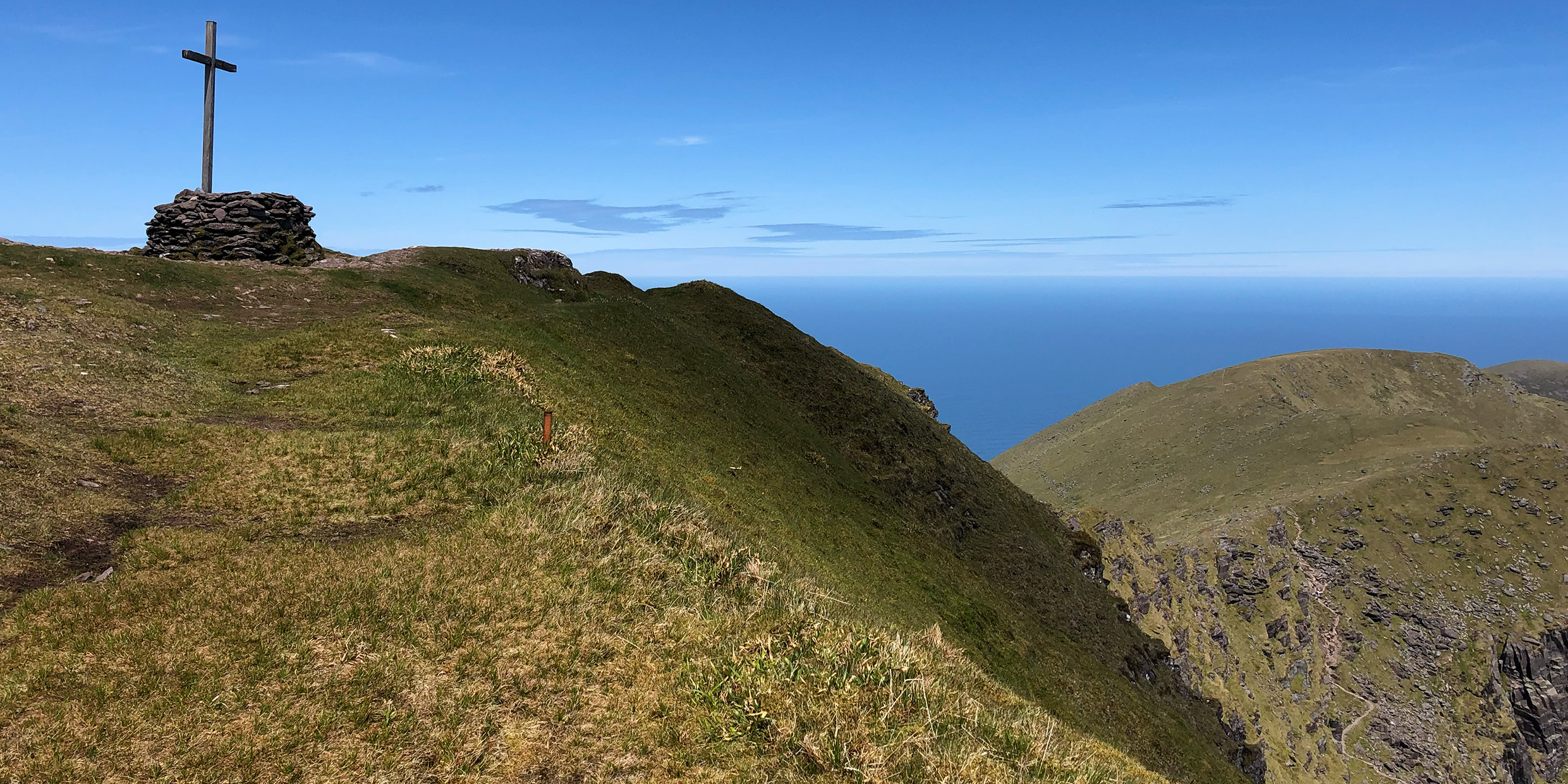 Image of a grass covered mountain with a Christian cross erected at the summit