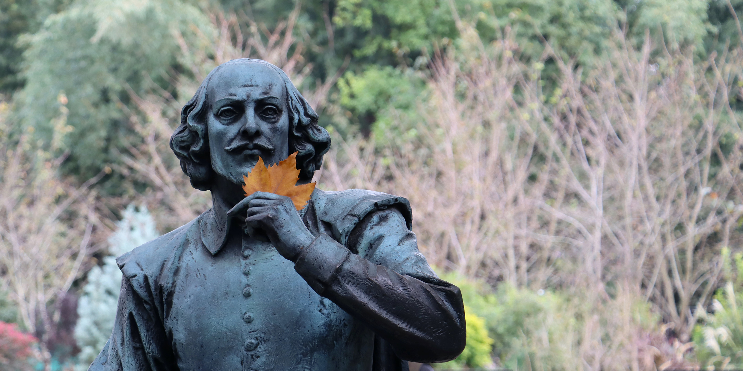 Image of a statue of William Shakespeare with a leaf from a tree placed into its lifted hand