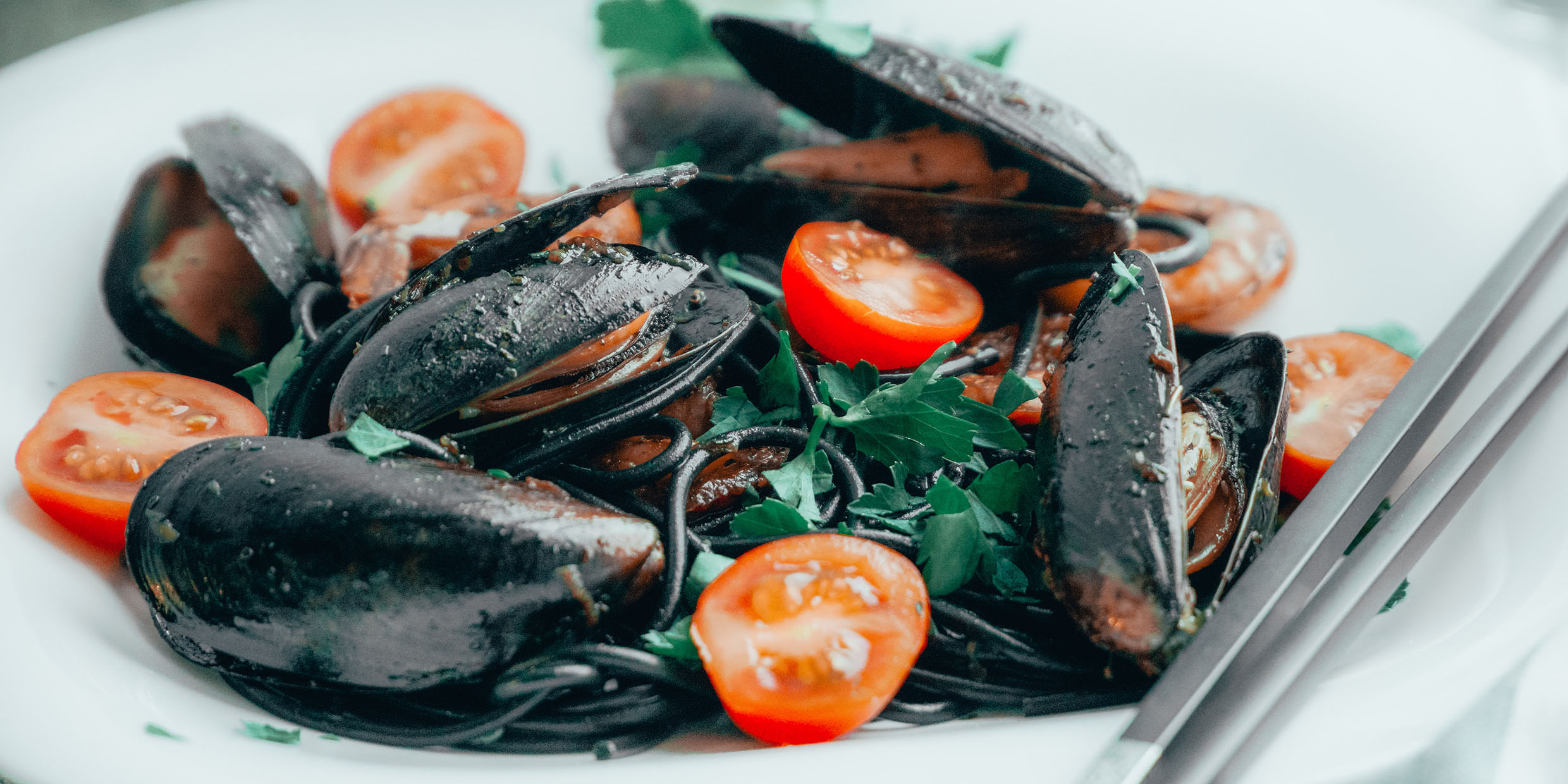 Image of a plate of mussels served with tomatoes and greens