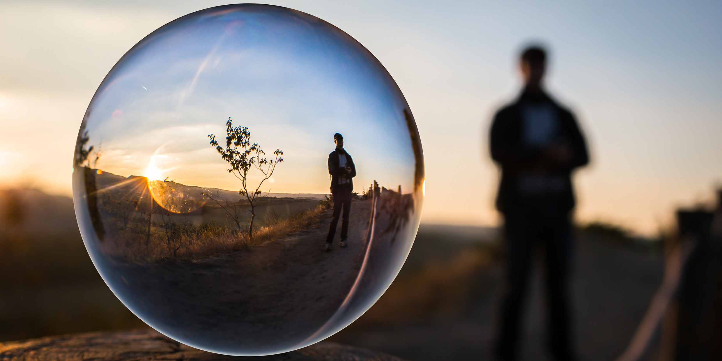 Image of standing man with his image refracted inside a glass sphere
