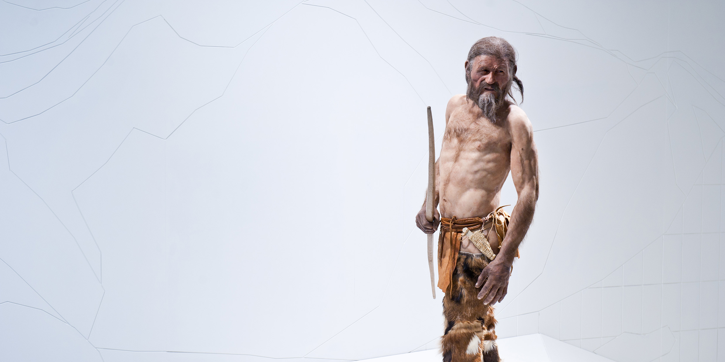 Image of a bare-chested man holding a wooden spear and wearing animal skins