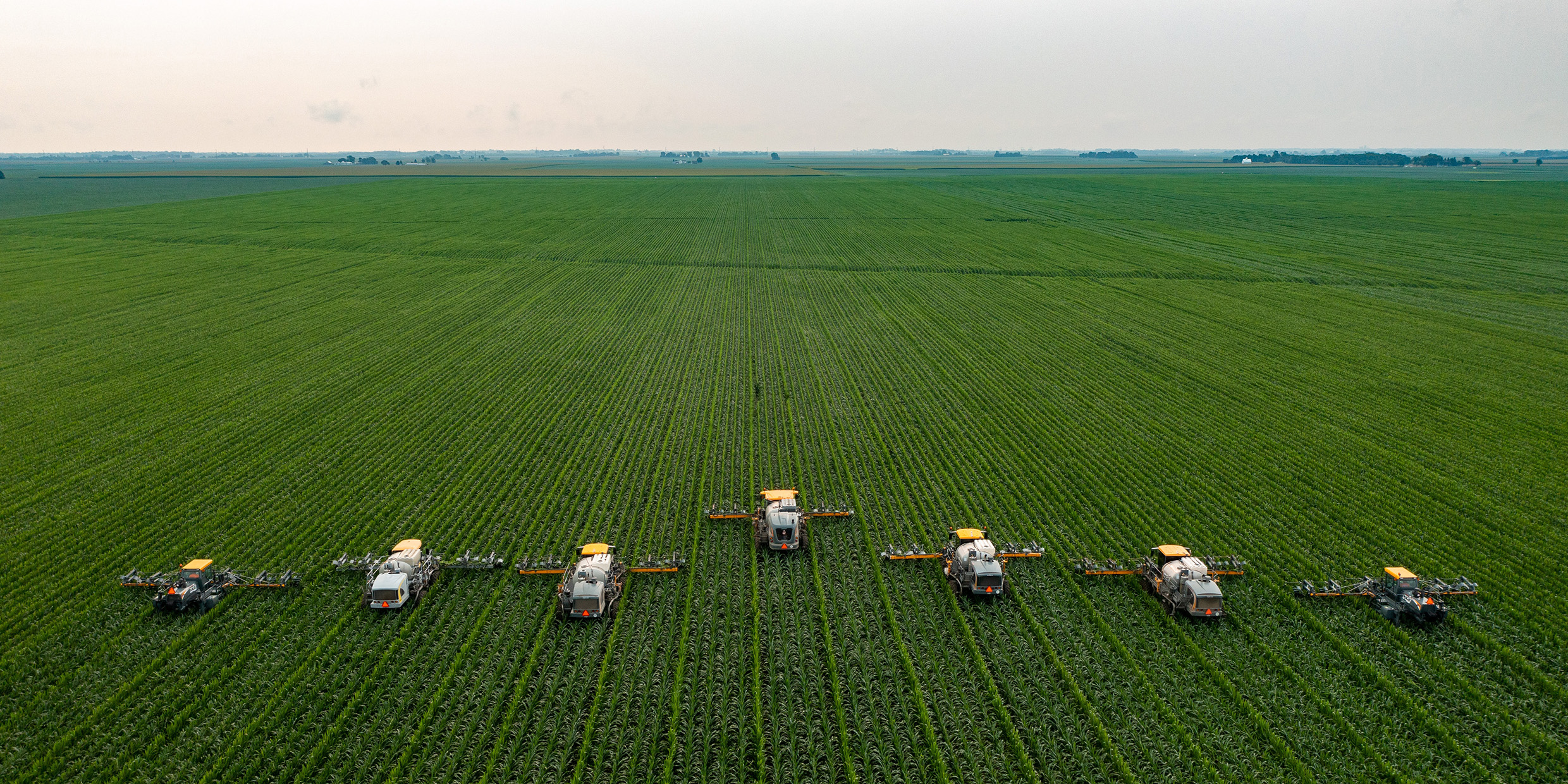 Image of a group of tractors harvesting a large field of crops