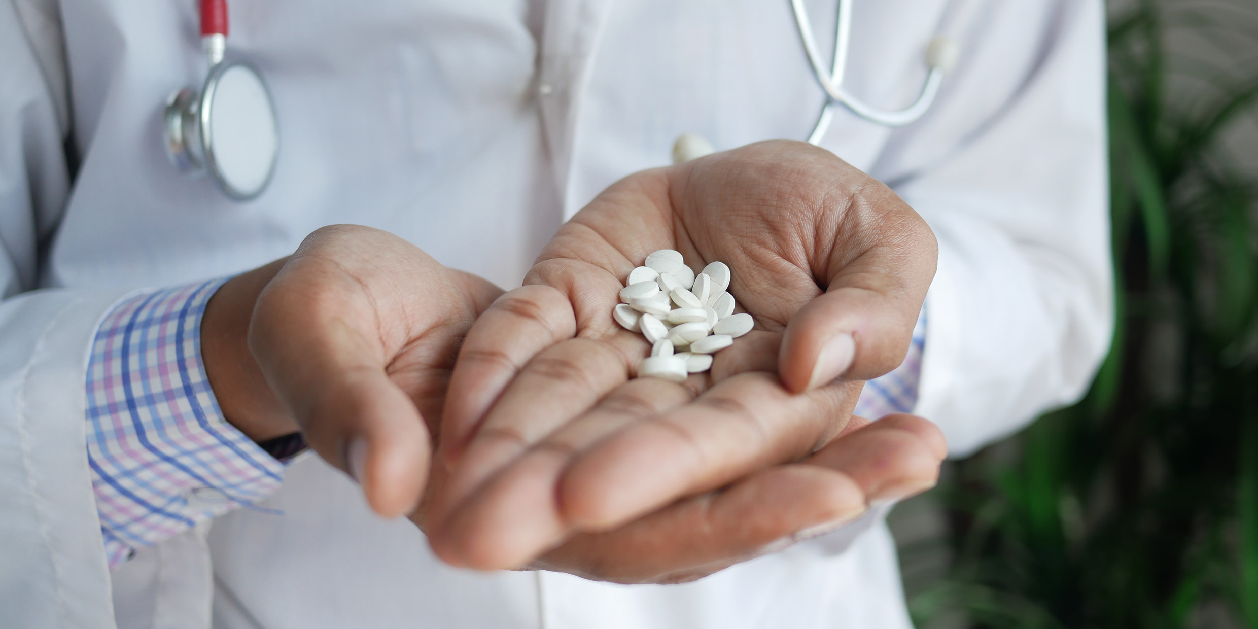 Image of a man wearing a white lab coat holding out a hand filled with white pills