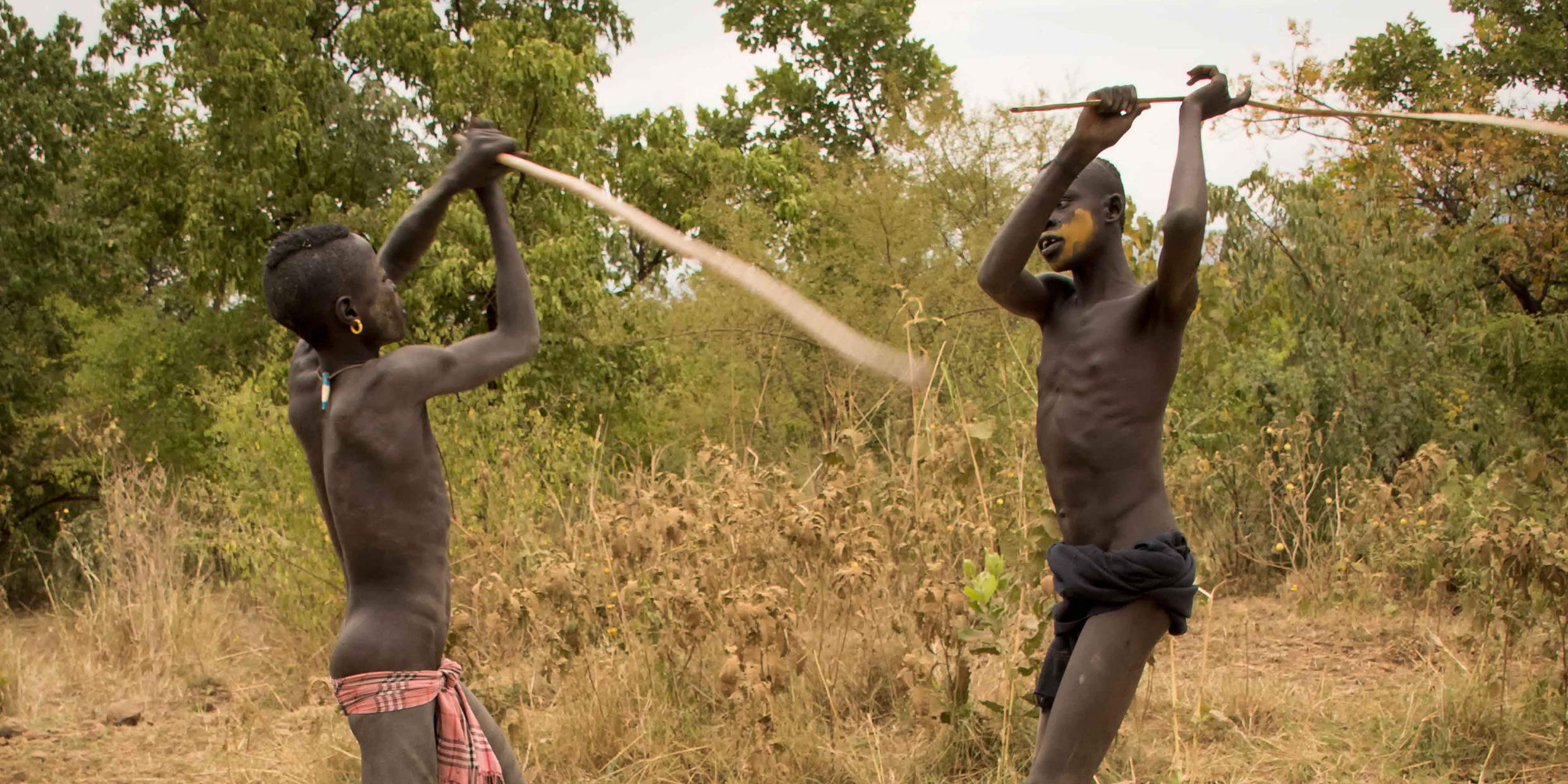 Image of two young men fighting with long thin sticks