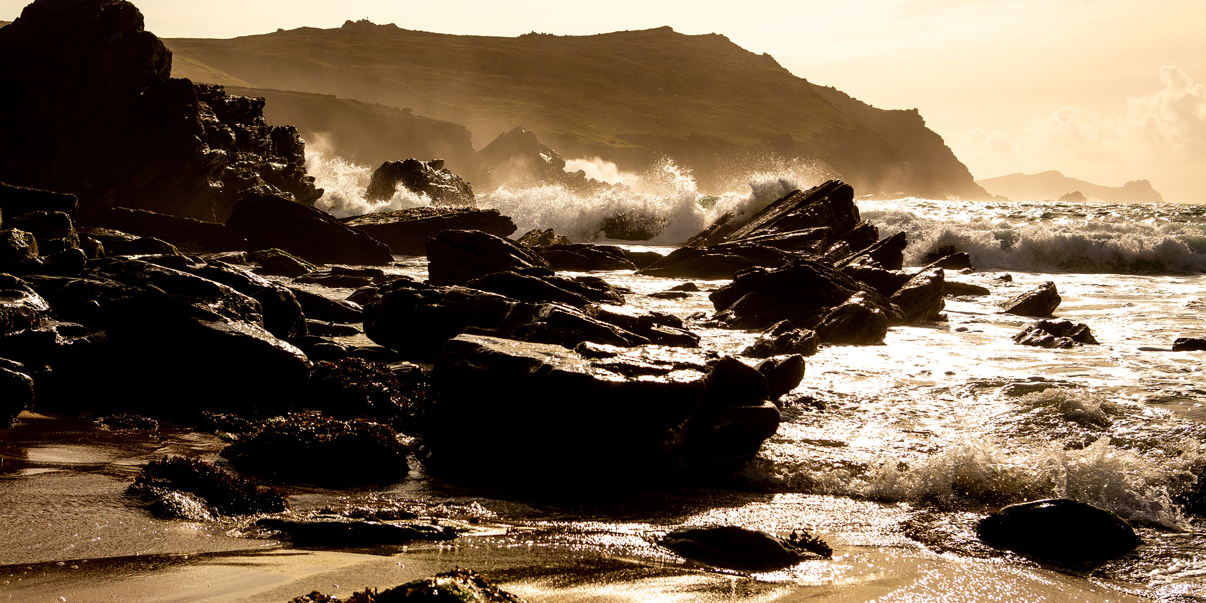 Image of water crashing on rocks in golden sunlight