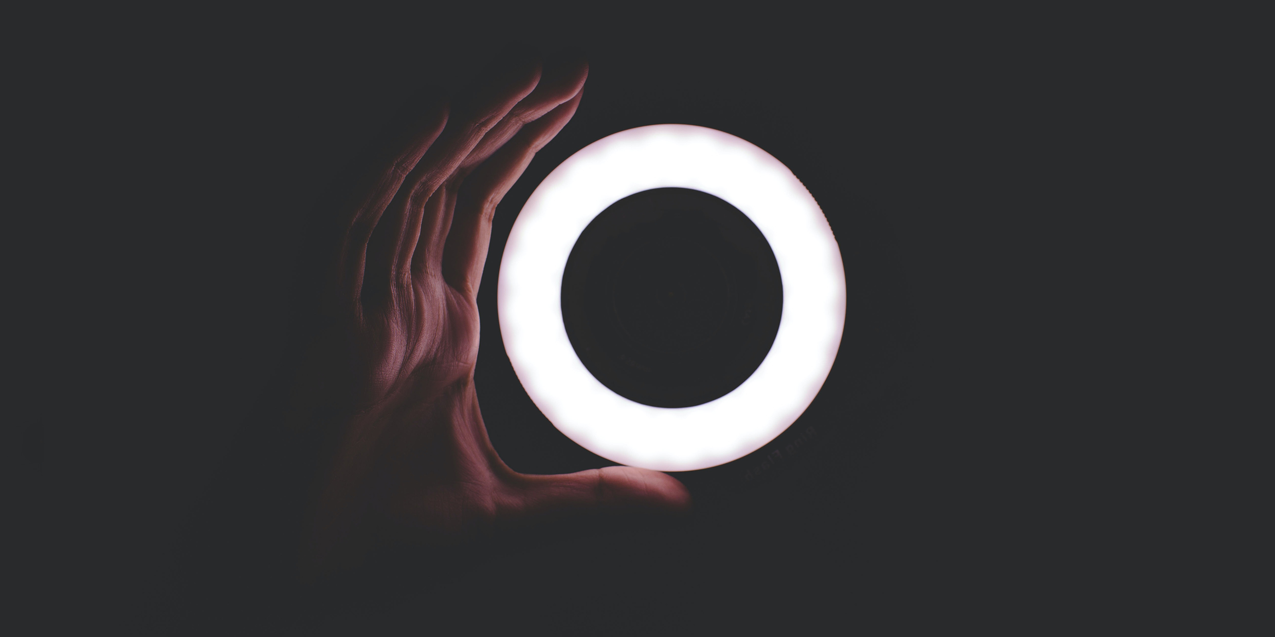 Image of a hand grasping for a glowing circle of light in a dark space