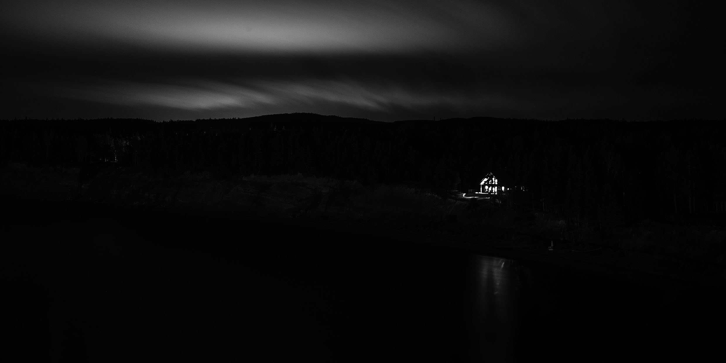 Black-and-white image of a single illuminated house in a dark night