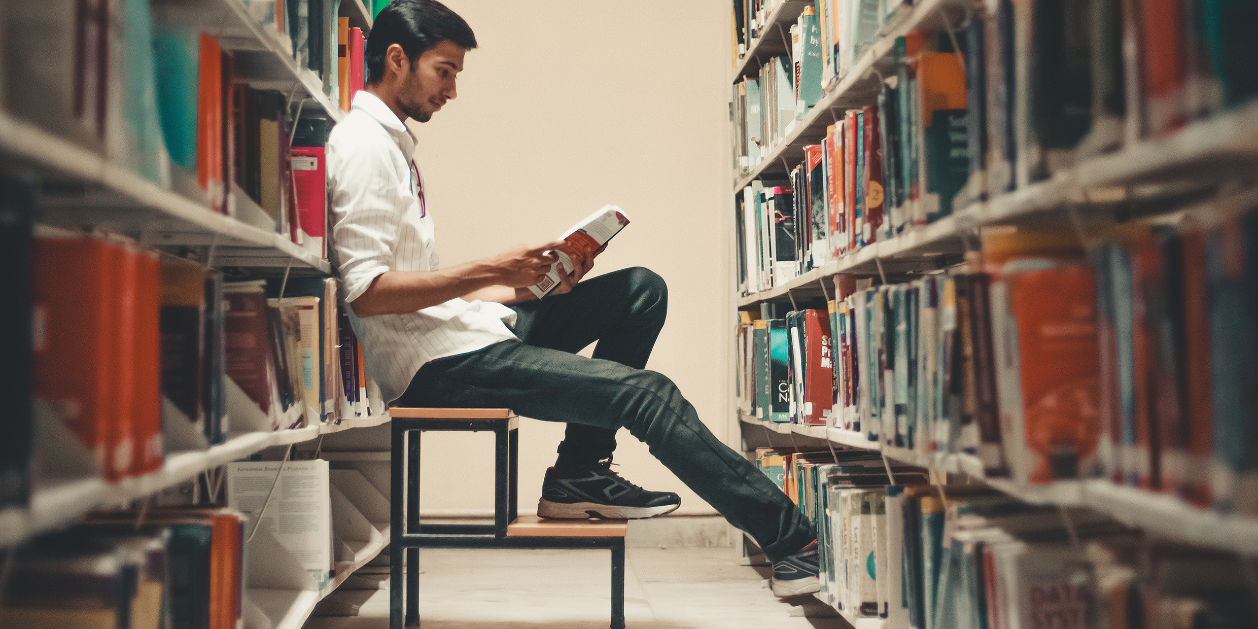 Image of a young man reading a book inside a library