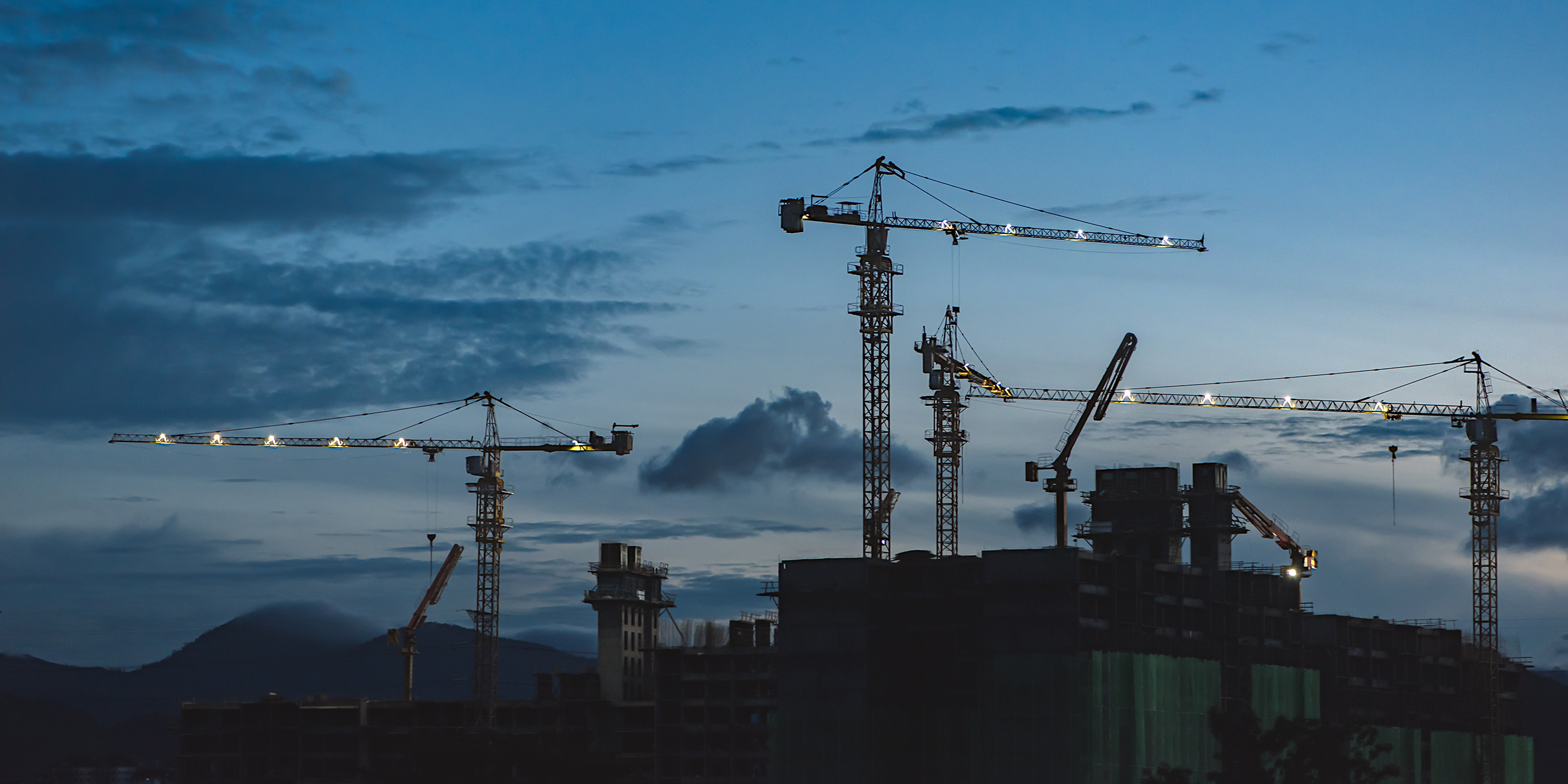 Image of construction cranes over a cityscape