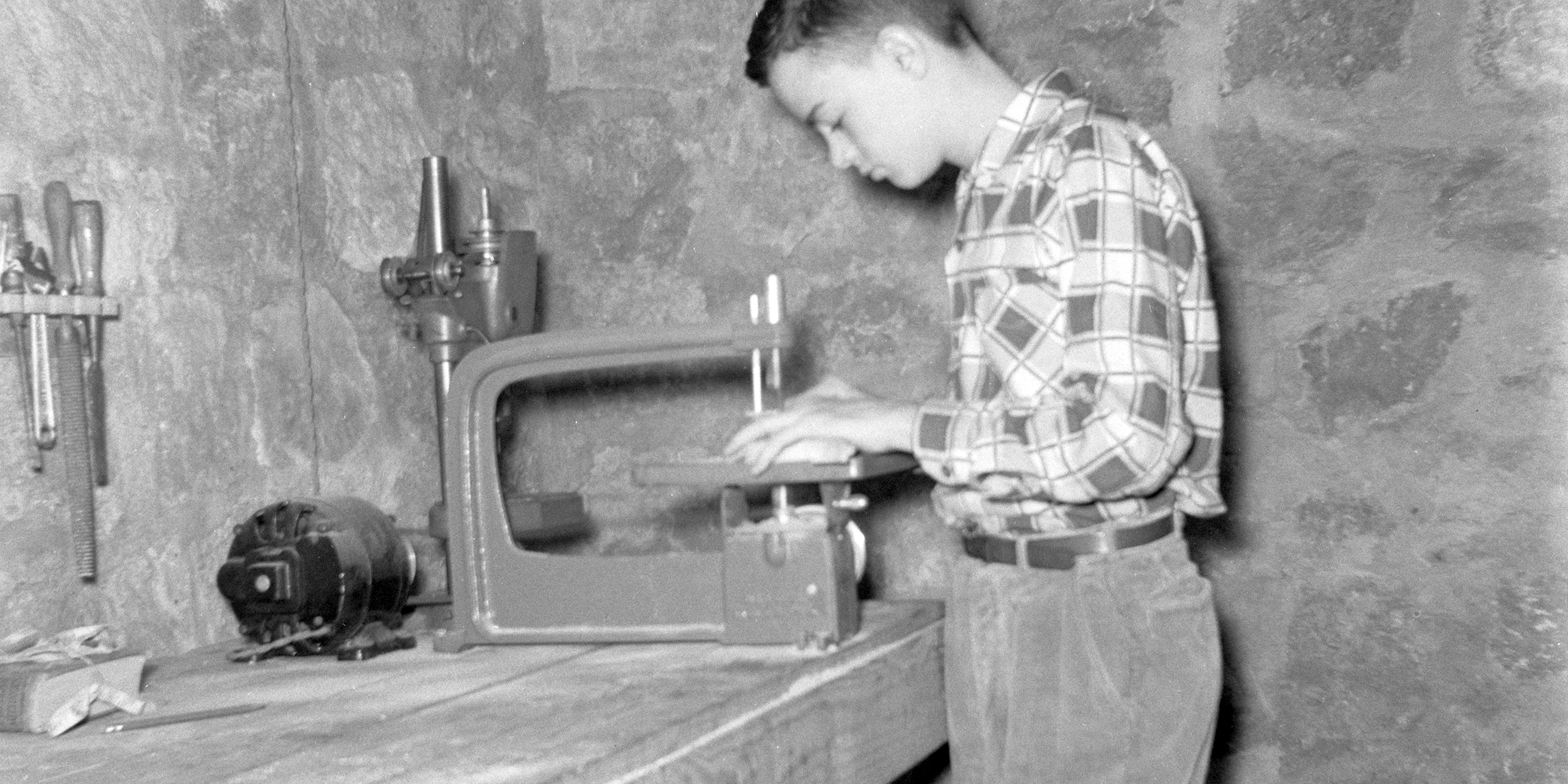 Image of a teenager cutting a board with a jigsaw on a basement workbench